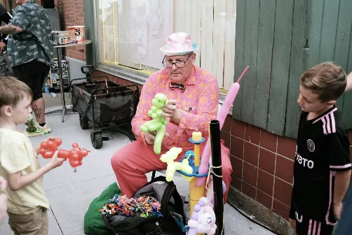 A balloon-twisting entertainer making balloon animals for kids on the street at Harvest
