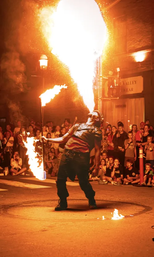 A fire performer breathing a plume of flame for a night-time street crowd at Harvest