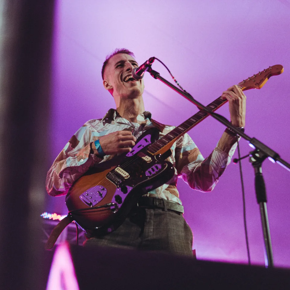 A guitarist laughing mid-song under magenta stage light at Harvest