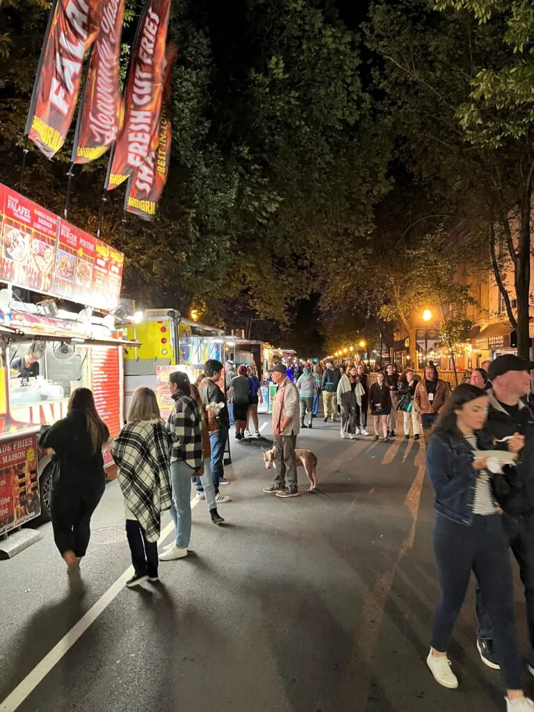 Food vendors and crowds filling the closed-off street at night during Harvest