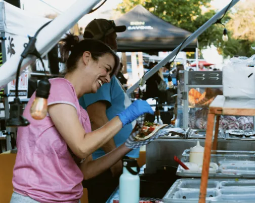A vendor plating food at a busy Harvest street-food stall