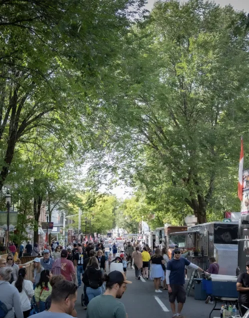 Crowds strolling the tree-lined downtown street past a row of food trucks at Harvest